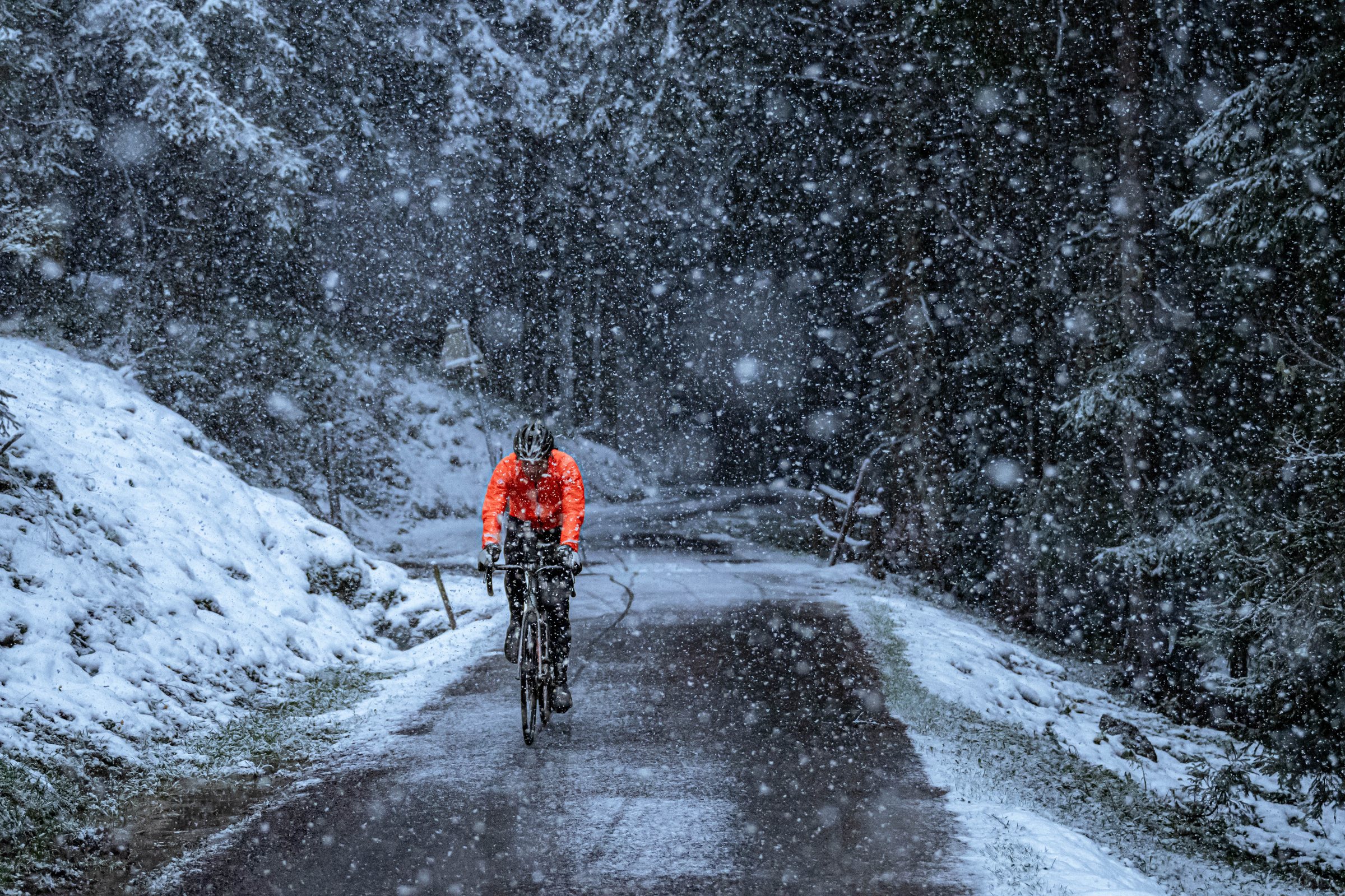 Rider in an orange jacket climbing a forest road in heavy snow during TURN02